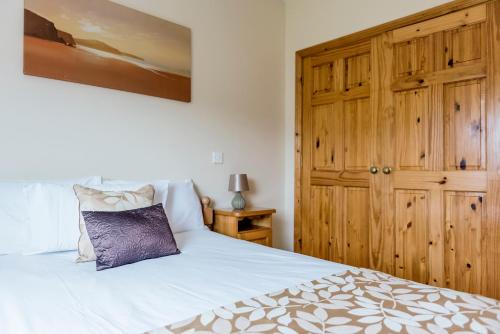 a bedroom with a white bed and a wooden cabinet at Portbeg Holiday Homes at Donegal Bay in Bundoran