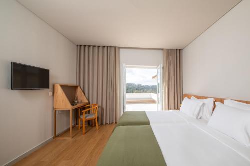 una camera d'albergo con letto, scrivania e TV di Montebelo Principe Perfeito Viseu Garden Hotel a Viseu