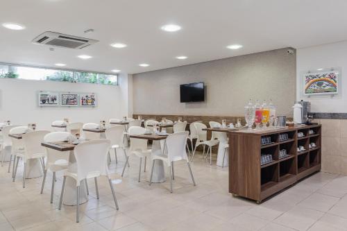 a restaurant with tables and white chairs and a tv at Citi Hotel Residence Caruaru in Caruaru