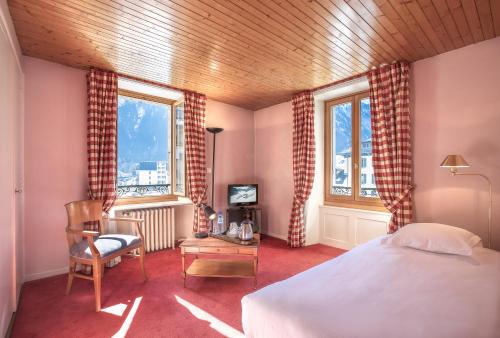 een slaapkamer met een bed en een stoel en 2 ramen bij La Croix Blanche in Chamonix-Mont-Blanc