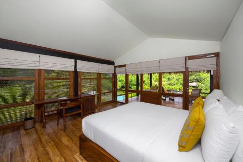 a bedroom with a bed and a desk and windows at Jetwing Kurulubedda in Galle