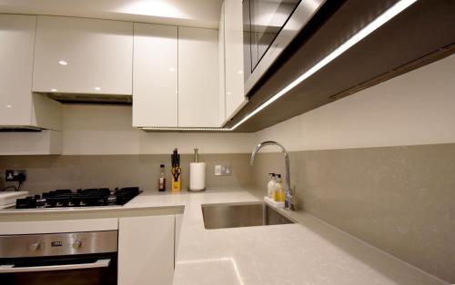 una cocina con armarios blancos y fregadero en Northside Apartments Ealing, en Londres