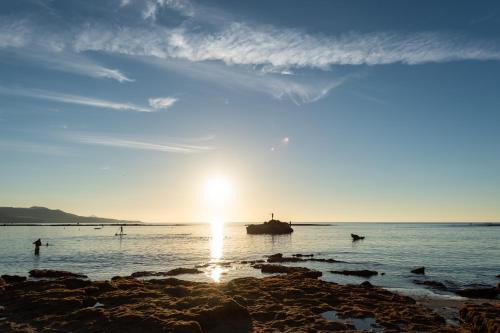 a sunset on the beach with people in the water at Living Las Canteras Homes - FRONT-LINE BEACH in Las Palmas de Gran Canaria
