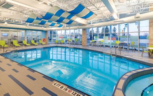 uma grande piscina num edifício com cadeiras e mesas em Holiday Inn Express & Suites - Saskatoon East - University, an IHG Hotel em Saskatoon