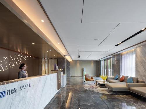 a lobby with couches and a person standing at a counter at Lavande Hotel National Sun Yat-sen University, Zhuhai in Zhuhai