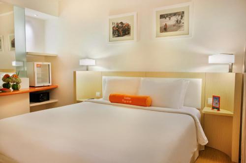 a bedroom with a large white bed with an orange pillow at HARRIS Hotel & Conventions Malang in Malang