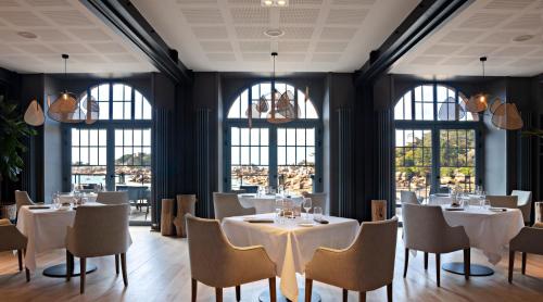 restauracja z białymi stołami, krzesłami i oknami w obiekcie Castel Beau Site w mieście Perros-Guirec
