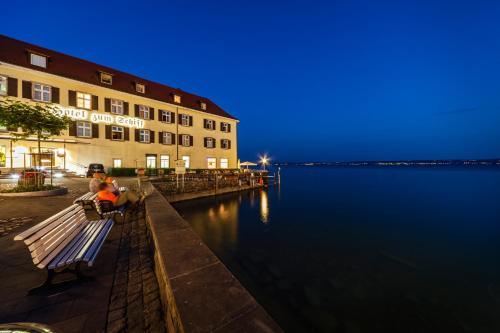 two people sitting on a bench next to a body of water at Flair Hotel zum Schiff in Meersburg