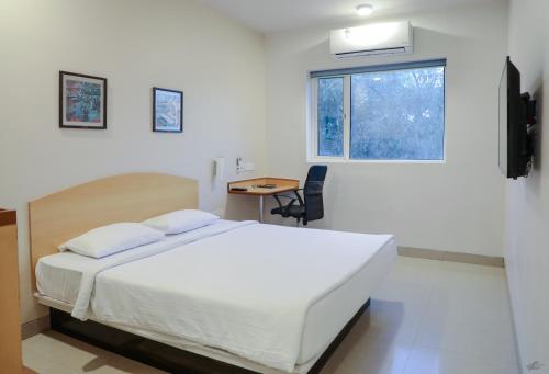 a bedroom with a bed and a desk and a window at Ginger Nashik in Nashik