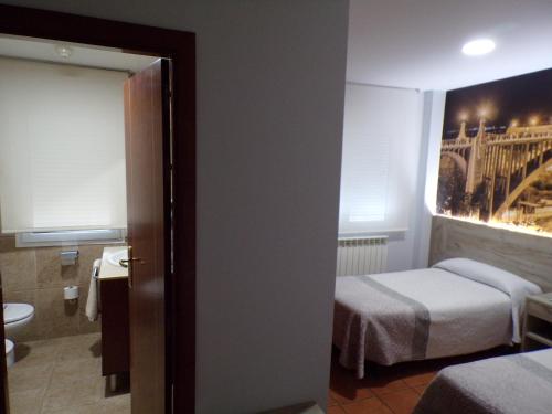 a room with two beds and a bathroom with a painting at Hostal Serruchi in Teruel