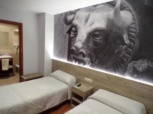 a room with two beds and a painting of a bull at Hostal Serruchi in Teruel