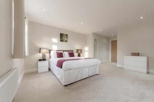 a white bedroom with a large bed and two lamps at Roomspace Serviced Apartments - Kinnaird Court in Esher
