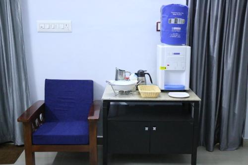 a table with a blue chair and a coffee maker on it at Hotel NKC Airport in Chennai