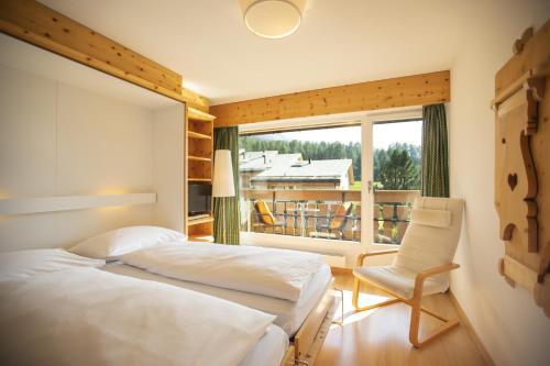 a bedroom with two beds and a chair and a window at Ferienwohnung Club House F4 in Surlej