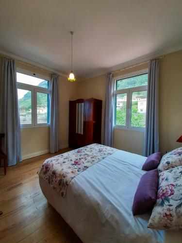 a bedroom with a large bed and two windows at Avó Lucindinha House - Porto Moniz in Porto Moniz