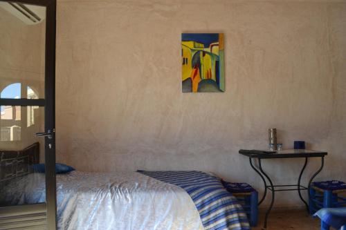 a bedroom with a bed and a table with a painting at Riad Dar Bergui in Ouarzazate