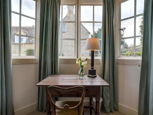 a table with a lamp and two chairs in a room with windows at The Old Dairy in Burford