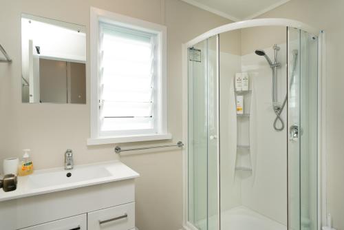 a white bathroom with a shower and a sink at Dove Cottage in Oneroa