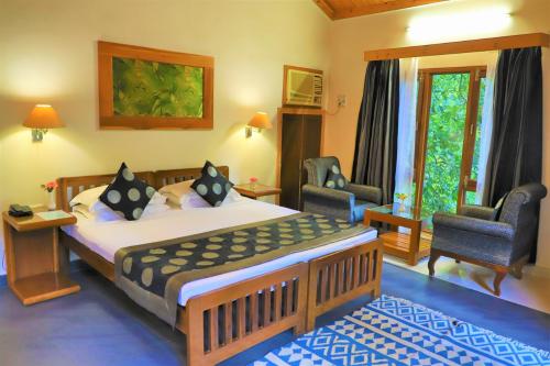 a bedroom with a large bed and two chairs at The Den Corbett Resort in Dhikala Zone