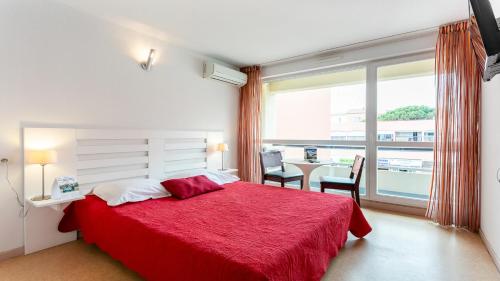 une chambre avec un lit rouge et une grande fenêtre dans l'établissement Vacancéole - Résidence Le Saint Clair, au Cap d'Agde