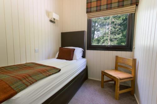 a bedroom with a bed and a chair and a window at Macdonald Lochanhully Resort in Aviemore