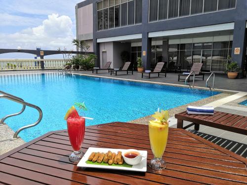 a table with two drinks on it next to a pool at Hotel Grand Continental Kuala Terengganu in Kuala Terengganu