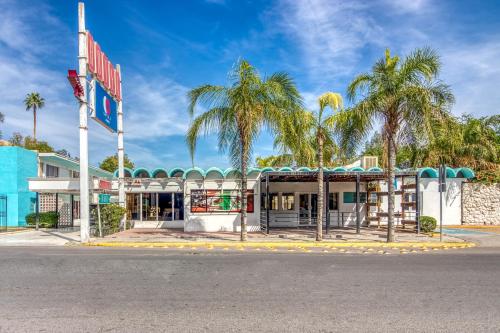 a building with palm trees in front of it at Capital O Hotel La Siesta, Gomez Palacio in Gómez Palacio