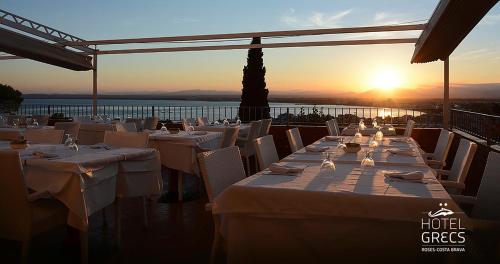 a restaurant with white tables and chairs and the sunset at Hotel Grecs in Roses