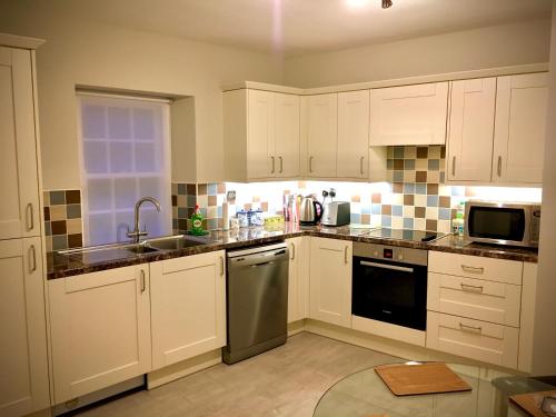 una cocina con armarios blancos y electrodomésticos de acero inoxidable en Peaceful 2 bedroom granite country dower house, en La Villaise