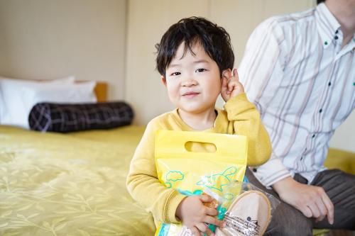 a young boy sitting on a bed with a bag at Hotel Dorf Shizuoka in Shizuoka