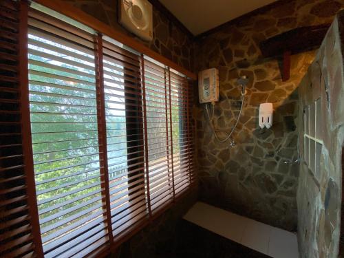 a bathroom with wooden blinds and a stone wall at Saiyok River House in Sai Yok