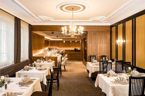 un restaurant avec des tables et des chaises blanches et un lustre dans l'établissement Hotel Touring Dolomites, à Santa Cristina Valgardena