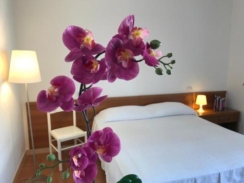 un vase d'orchidées violettes assis à côté d'un lit dans l'établissement Grazioso appartamento a due passi dal mare, à Cervia