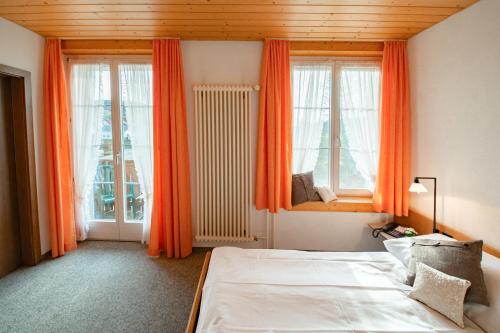 Schlafzimmer mit einem Bett und Fenstern mit orangefarbenen Vorhängen in der Unterkunft Hotel Restaurant Bad Gutenburg in Lotzwil