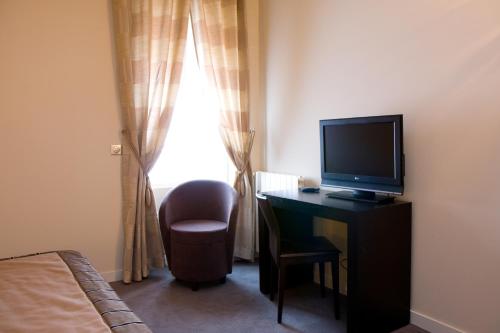 um quarto com uma secretária, uma televisão e uma cadeira em Grand Hôtel d'Orléans em Toulouse