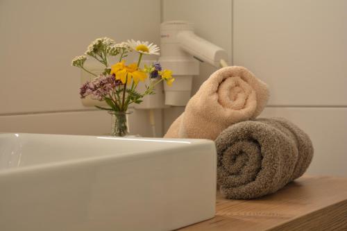 a bathroom sink with towels and a vase of flowers at Hotel Garni Alpina in Damuls