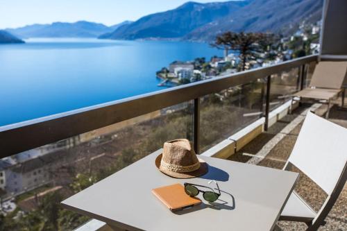 a hat and sunglasses on a table with a view of a lake at Parkhotel Brenscino Brissago in Brissago