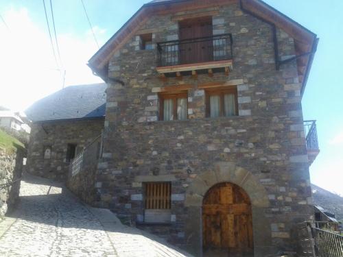 a stone house with wooden doors and a balcony at Casa Feixas in Gistaín