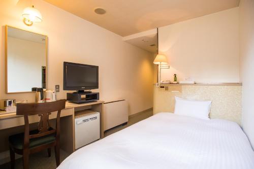 a hotel room with a bed and a desk with a television at Kijima Kogen Hotel in Beppu