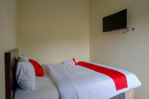 a bed with red and white sheets and a television on a wall at RedDoorz near Terminal Mendolo Wonosobo in Wonosobo