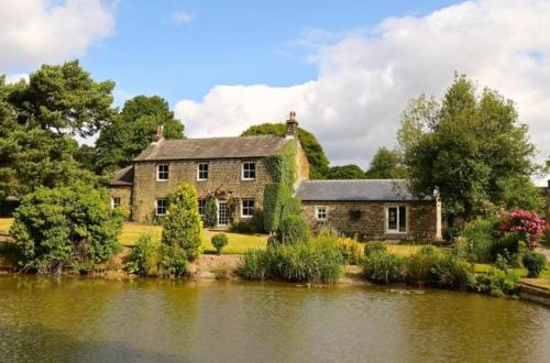 an old house next to a body of water at Woodsome Hall Golf Club Cottage on the Course in Fenay Bridge