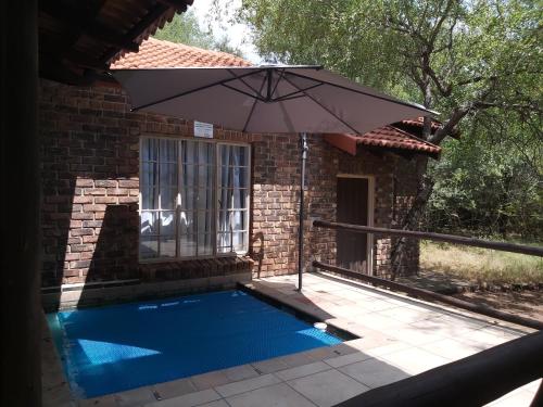 a swimming pool with an umbrella next to a house at Peace@Kruger in Marloth Park