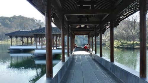 a pavilion over a lake with a person sitting on the dock at Hangzhou JiuYueJi Bed&Breakfast in Hangzhou