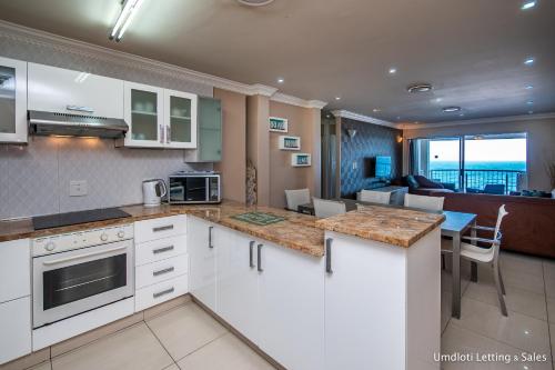 a kitchen with white cabinets and a living room at Cozumel 411 in Umdloti