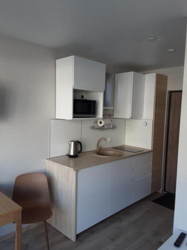 eine Küche mit weißen Schränken, einer Spüle und einer Mikrowelle in der Unterkunft Studija GRaDO2 in Juodkrantė