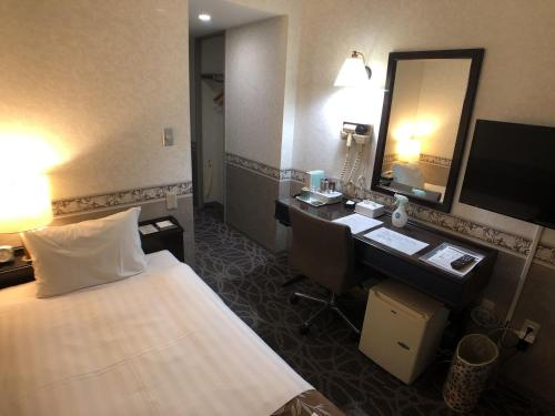 a hotel room with a bed and a desk and a mirror at Hotel Crown Hills Kamaishi in Kamaishi