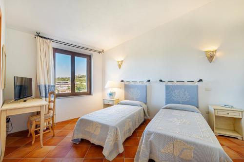 two beds in a room with a desk and a window at Hotel San Trano in Luogosanto