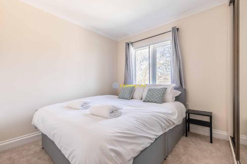 a bedroom with a bed with white sheets and a window at Heathrow Apartment - private balcony & FREE PARKING! in Slough