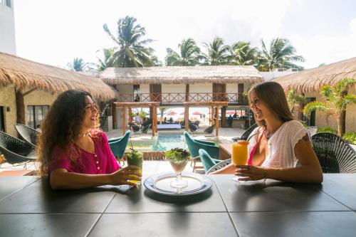 dos mujeres sentadas en una mesa con bebidas en Kinta Kan Beach Hotel Boutique Playa del Carmen en Playa del Carmen