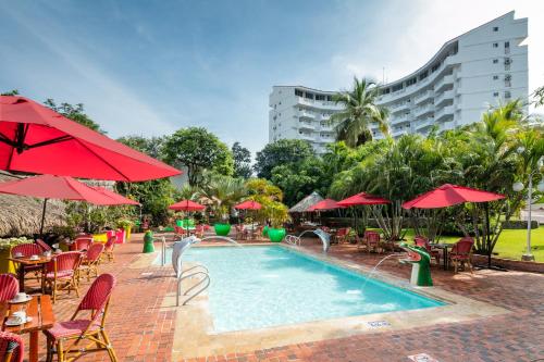 una piscina con mesas, sillas y sombrillas rojas en Decameron Galeon - All Inclusive en Santa Marta